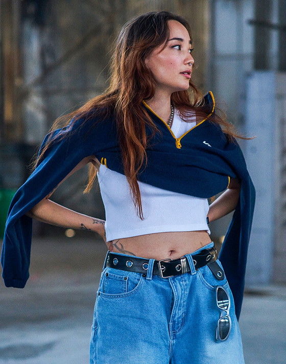 A young woman poses in a warehouse with a white Vans rib tanktop and a navy quarter-zip.