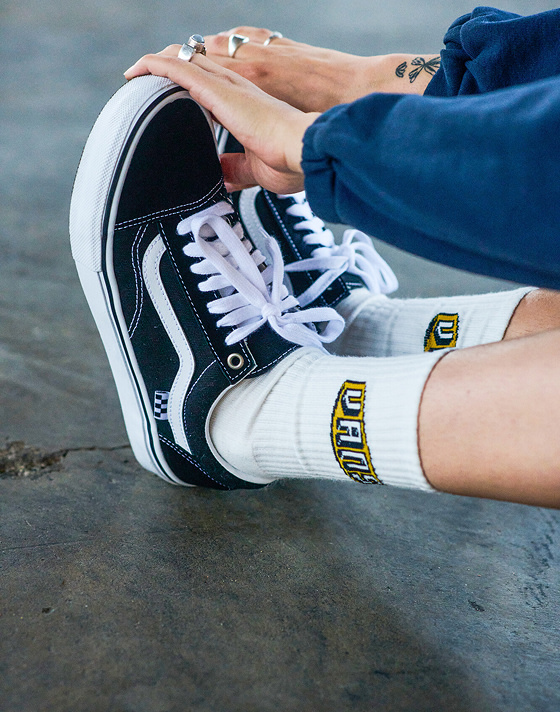 A person stretches and touches their toes in white Vans crew socks and black and white Old Skool.