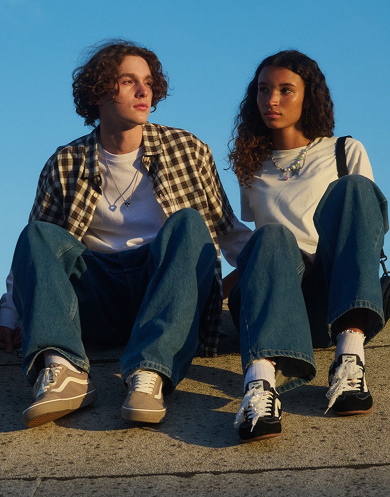 A young boy and girl sit on a roof in Vans clothes, beige Old Skool, and black Super Lowpro.