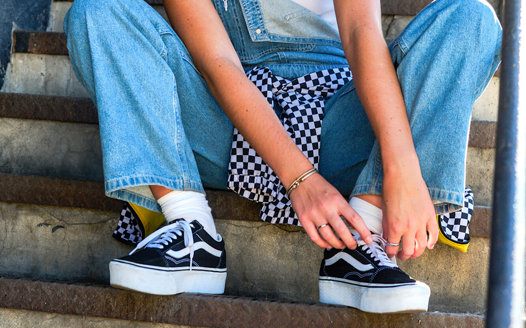 A woman laces up her Platform Old Skool on a concrete staircase wearing a white Drew Rib Tank Top and denim blue Sirelle Overalls.