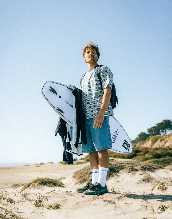 Vans Surf Team Rider Micky Clarke holds a surfboard on a beach wearing coal brown UltraRange 2.0 on a sunny day.