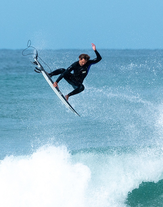 Vans Surf Team Rider Micky Clarke catches air off a wave and holds his surf in a spray of ocean water.
