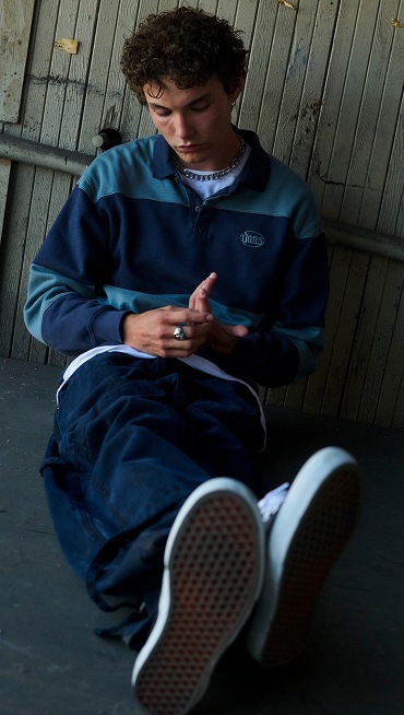 A man sits on the floor wearing a light blue and navy rugby-style polo.