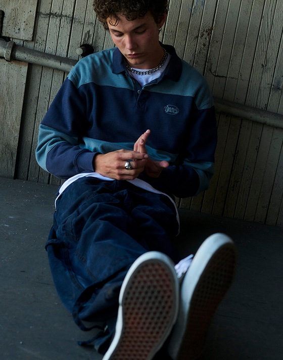 A man sits on the floor wearing a light blue and navy rugby-style polo.