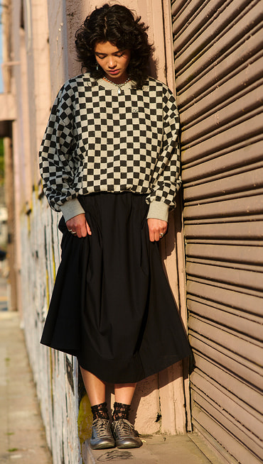 A young woman wearing a black Francesca Full Skirt and the Checkerboard Retro Crew Sweatshirt looks down at her black and silver Super Lowpro.