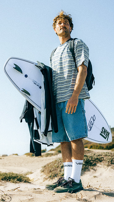 Vans Surf Team Rider Micky Clarke holds a surfboard on a beach wearing coal brown UltraRange 2.0 on a sunny day.