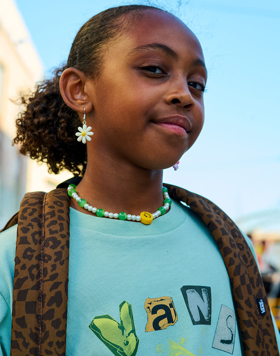 A girl looks into the camera wearing a Dachsund Brown Old Skool Classic Backpack and a mint green Vans graphic t-shirt.