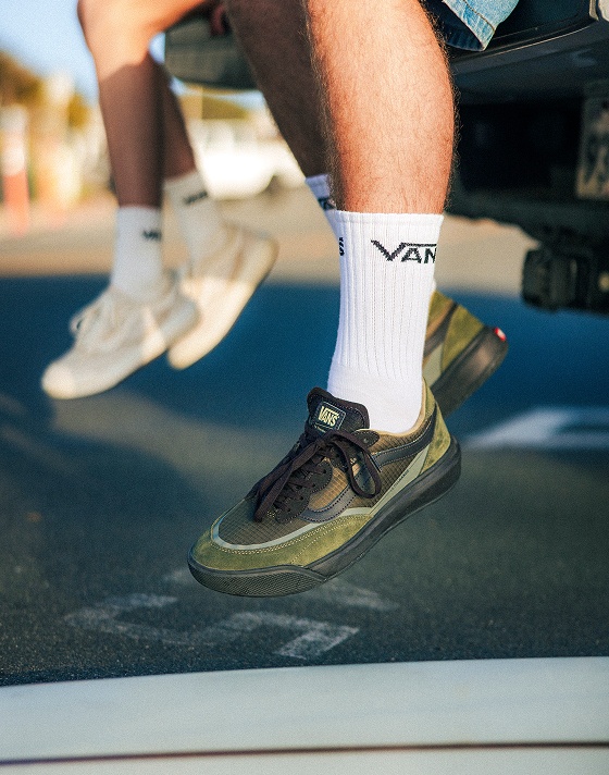 A young man and woman sit on a truck in a parking lot wearing UltraRange 2.0 with surfboards on the concrete and the beach in the background.