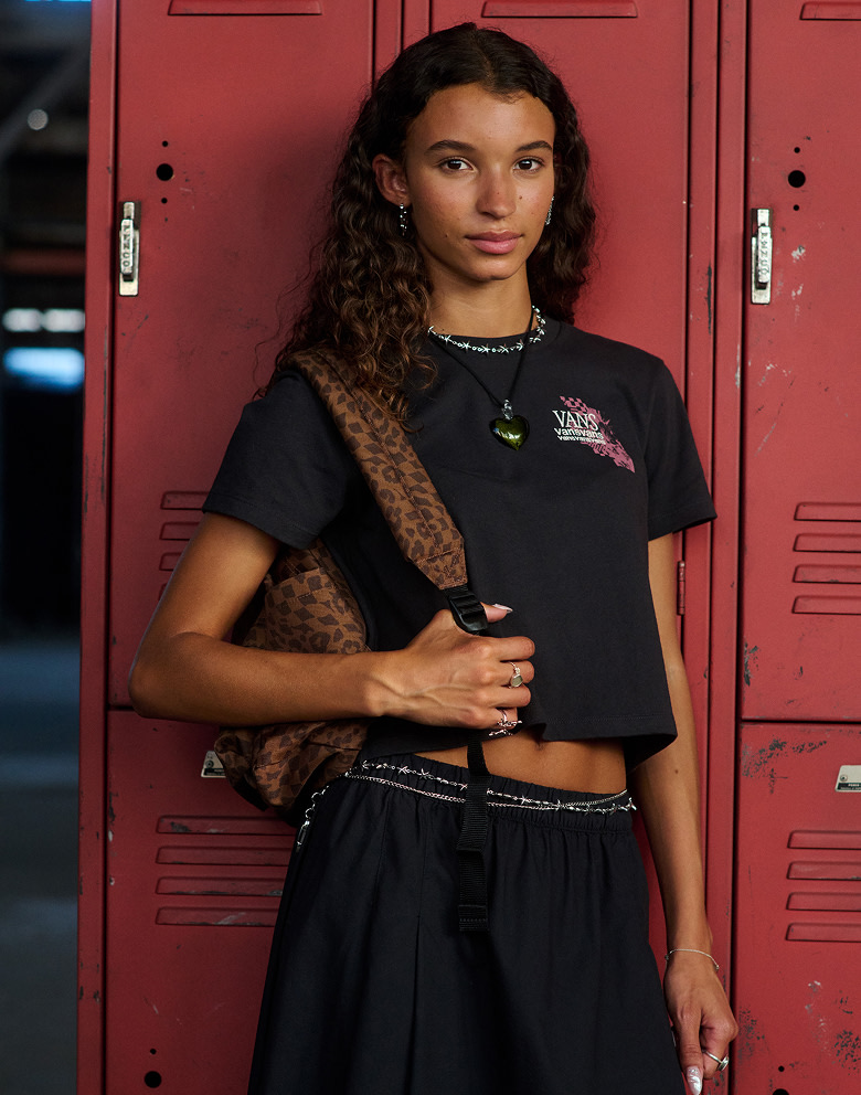 A close-up of a girl with a Dachshund Brown Old Skool Classic Backpack and Vans clothes leaning against a locker.