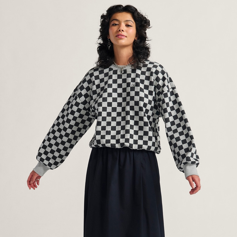 A young woman wearing a black Francesca Full Skirt and the Checkerboard Retro Crew Sweatshirt poses in a photography studio.