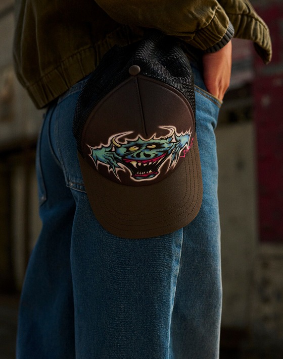 A close-up of a black Vans trucker hat hanging by someone’s belt loop in a warehouse.