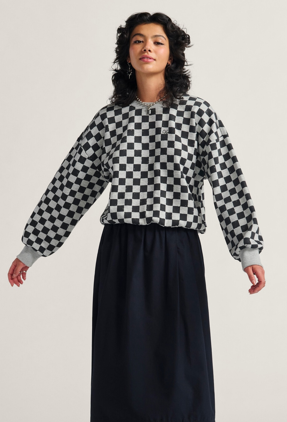 A young woman wearing a black Francesca Full Skirt and the Checkerboard Retro Crew Sweatshirt poses in a photography studio.