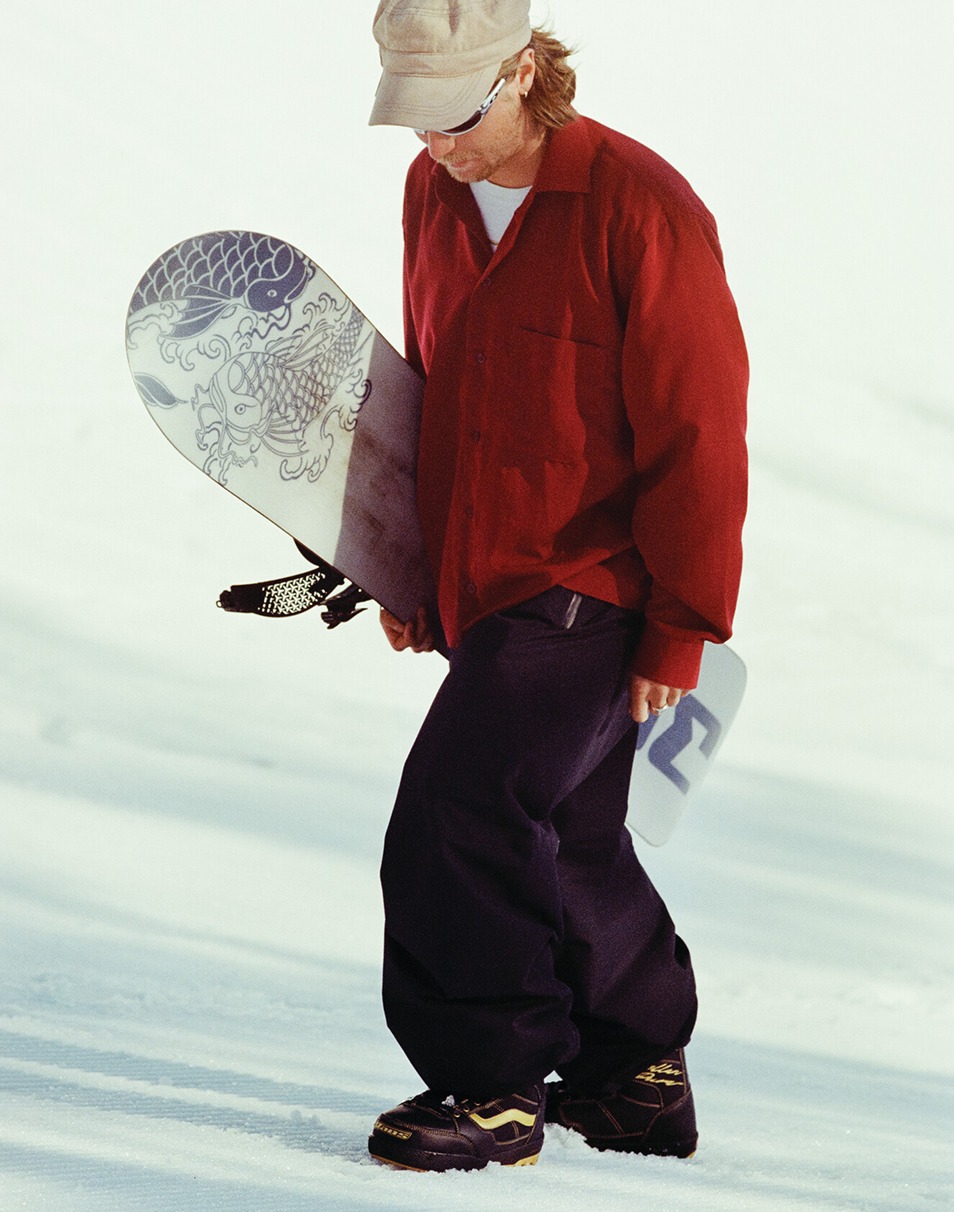 Vans Snowboard Team Rider Rene Rinnekangas holding his snowboard and walking up a snow-covered slope in the Invado Pro.