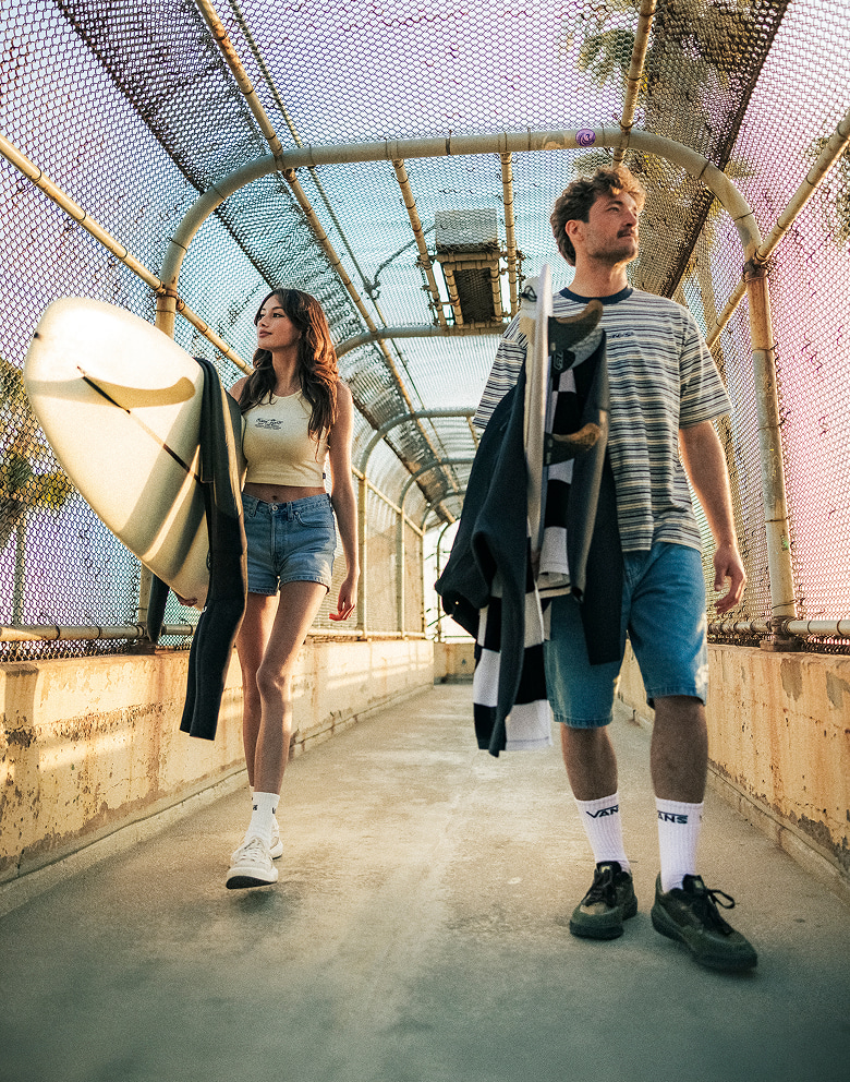 Vans Surf Team Riders Maddie Miller and Micky Clarke crossing a pedestrian bridge holding surfboards and wearing the UltraRange 2.0.