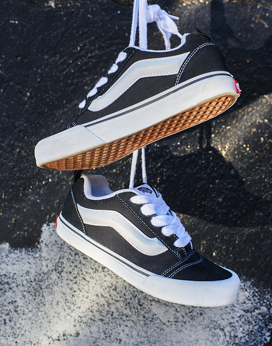 A pair of black and white Knu Skool hang from their laces on a wall.