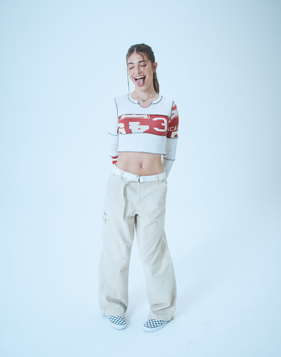 Gracie, a director, poses with her tongue out wearing a crop top and stargazer blue Premium Classic Slip-On Checkerboard Shoe on Open Set Los Angeles.