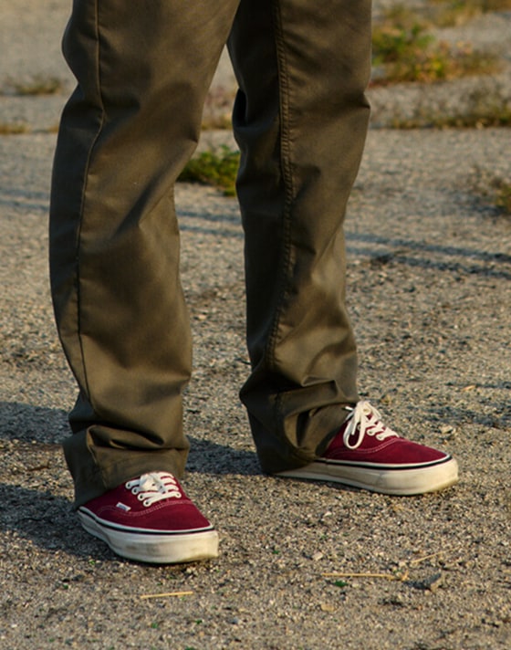 A knee-down shot of a man wearing burgundy Authentic shoes during golden hour.