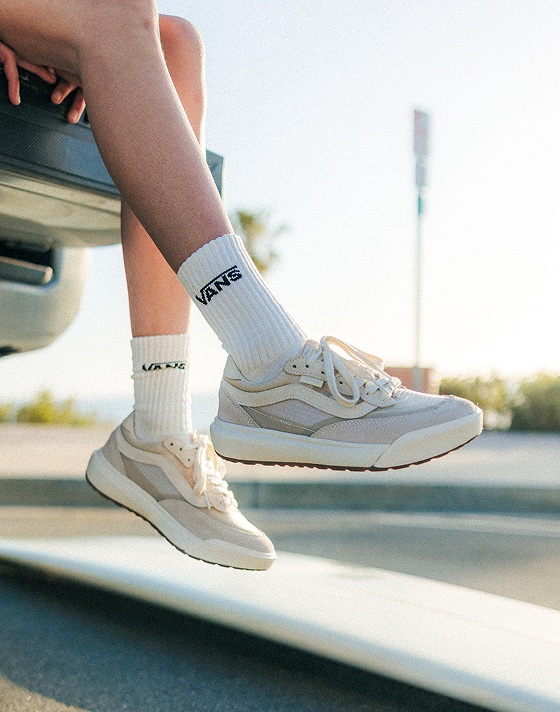 A close-up of Vans Surf Team Rider wearing Vintage White UltraRange 2.0 as she sits on a truck bed near a beach.