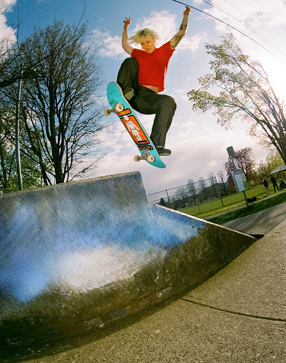 Vans Skate Team Rider Breana Geering hits a jump near a park wearing black Skate Slip-On in a grainy photo.
