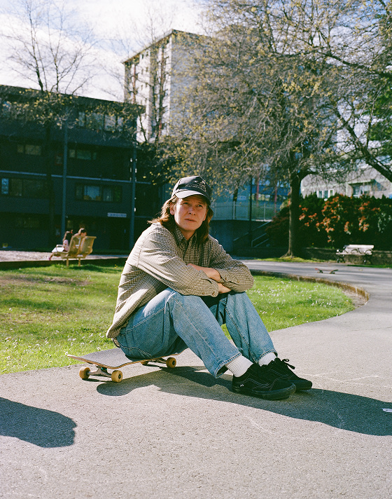 Vans Skate Team Rider Dustin Henry sits on a skateboard in a park wearing the all-black Skate Old Skool.