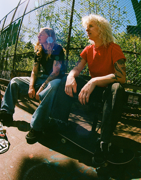 Vans Skate Team Rider Breana Geering sits on a park bench next to Vans Skate Team Rider Una Farrar wearing the all-black Skate Slip-On.