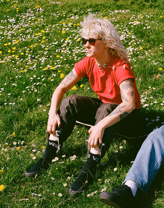 Vans Skate Team Rider Breana Geering sits on a skateboard in the grass wearing the all-black Skate Slip-On.