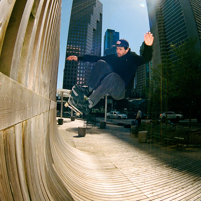 Vans Skate Team Rider Rick McCrank ollies off a wall in a city center wearing black Skate Old Skool shoes.