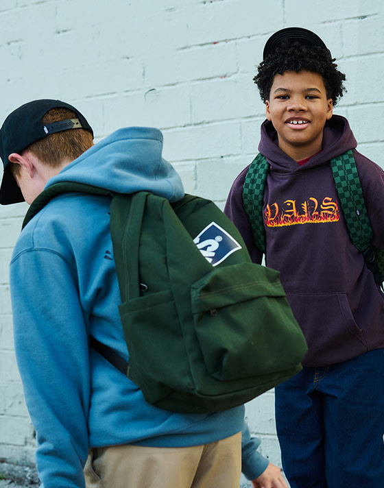 Two boys hang out wearing a green Old Skool Checkerboard Backpack and a green Kids Old Skool Grom Backpack.