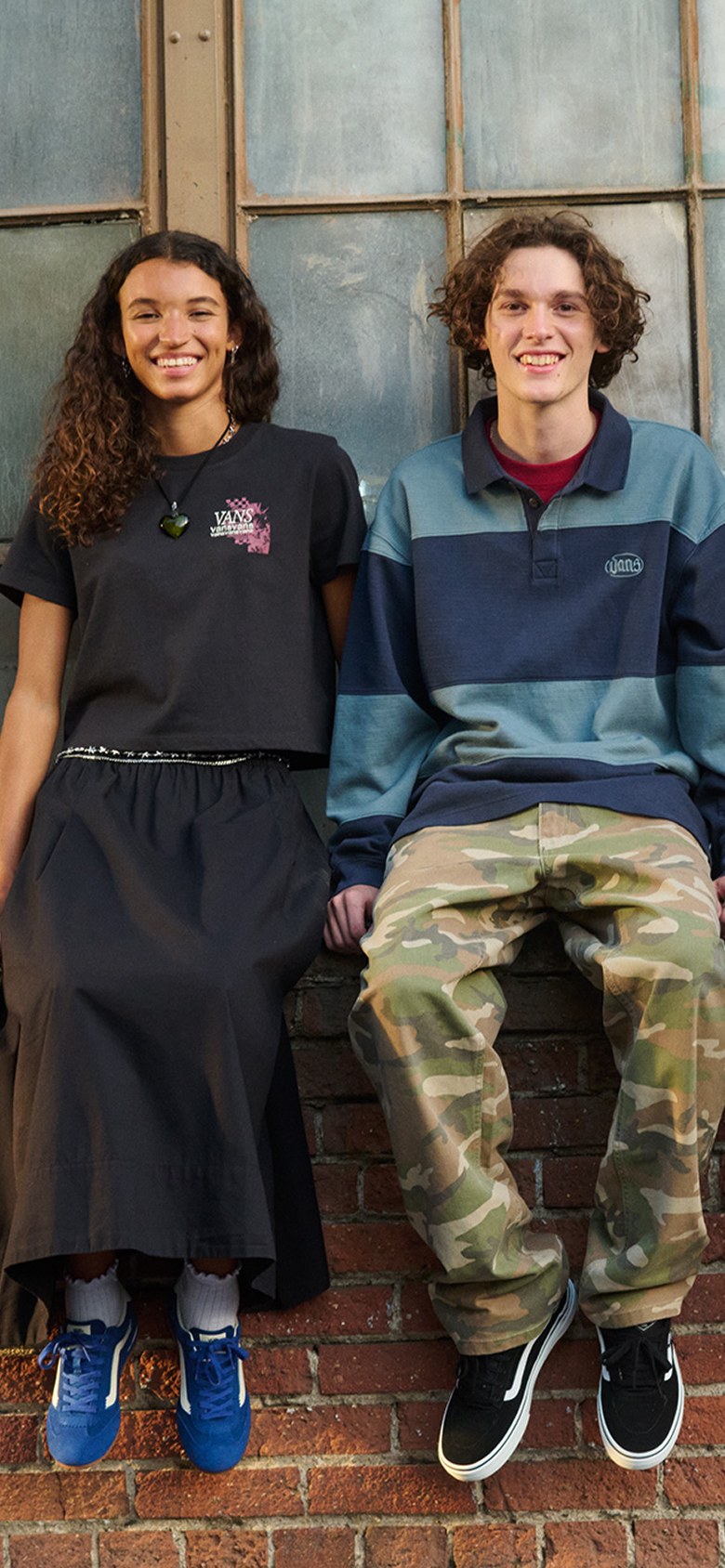 Two kids outside of a warehouse wearing the Francesca Full Skirt, the camo Drill Chore Carpenter Loose Pants, and the Bowman Rugby Long Sleeve Shirt.