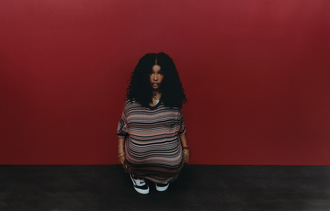 SZA sitting the ground with her knees tucked under her shirt.