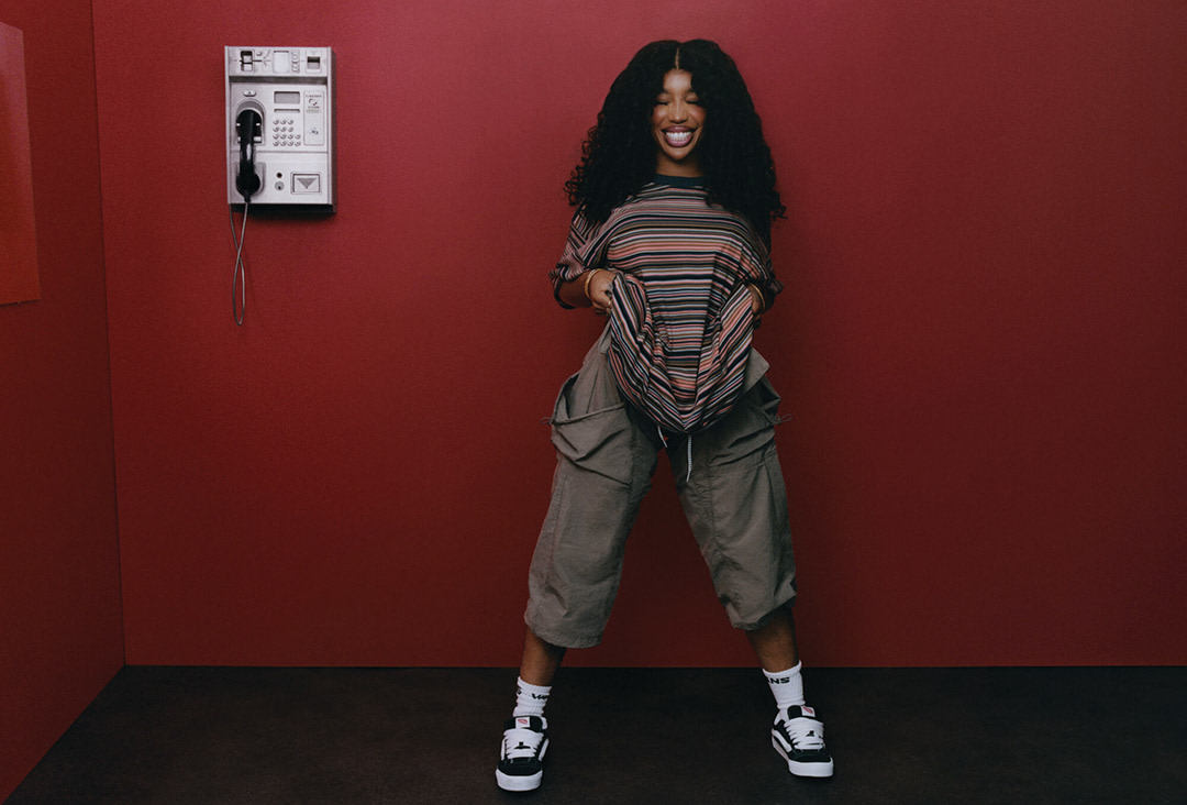 SZA standing next to a red wall with a way phone.