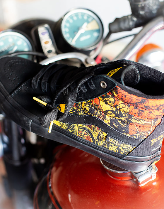A black Sk8-Hi with an orange and yellow illustration around the sides and heel from the Born Free Motorcycle Show rests on a motorbike.