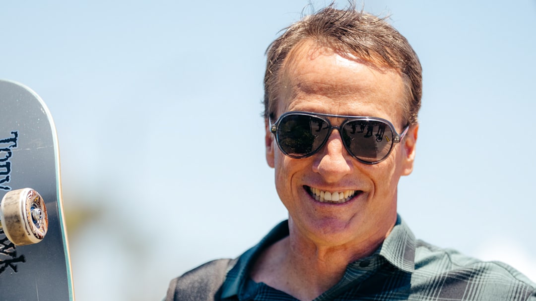 Tony Hawk smiling and wearing aviator sunglasses on a sunny day.