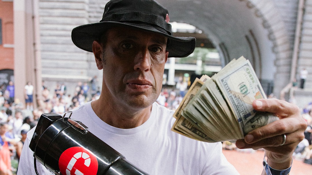 Steve Rodriguez holding a microphone and cash in the other hand at Go Skateboarding Day 2025 at the Brooklyn Banks.