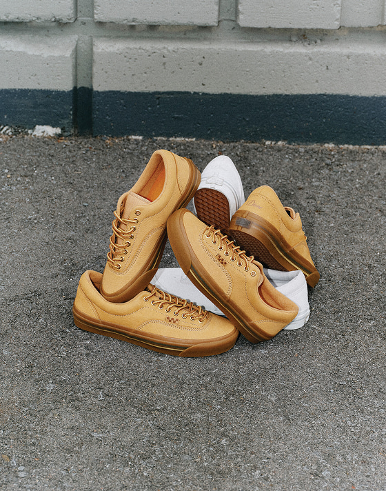 Plusieurs paires de Skate Era Stub blanches et dorées de Dime empilées sur un trottoir.