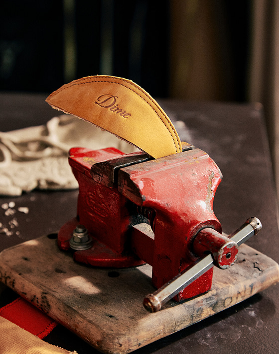 Le contrefort d’une Skate Era Stub dorée de Dime dépasse d’un étau dans un atelier, avec le logo cursif de Dime.