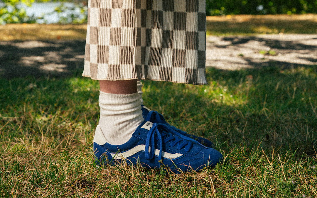 A knee-down shot of someone wearing blue Super Lowpro and a Checkerboard skirt in a park.