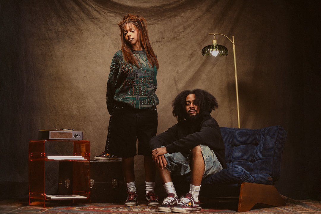 Two people in casual streetwear wearing Vans sneakers in a vintage room.