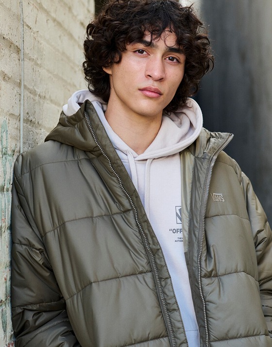 A man looks into the camera wearing a taupe mist Stockpile Pullover Hoodie and brown MTE Hillgate Puffer.
