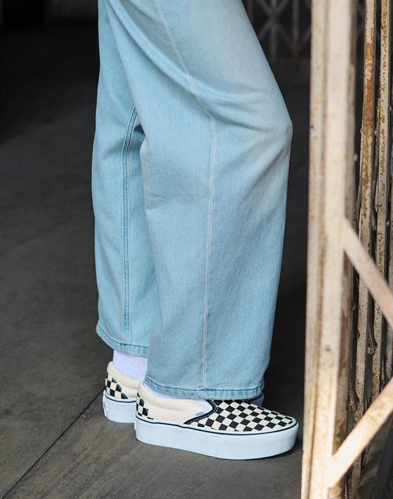 A waist-down shot of a woman wearing Classic Slip-On Checkerboard Platform shoes with Check-5 Baggy Denim Pants.