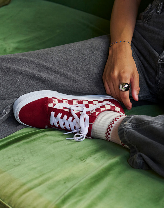 A close-up of a red Checkerboard Old Skool paired with gray jeans.