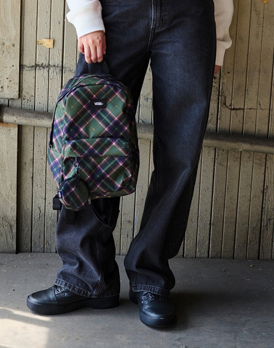 A woman poses outside a warehouse with a mauvewood MTE Hillgate Cropped Vest and a pine forest Old Skool Mini Backpack.