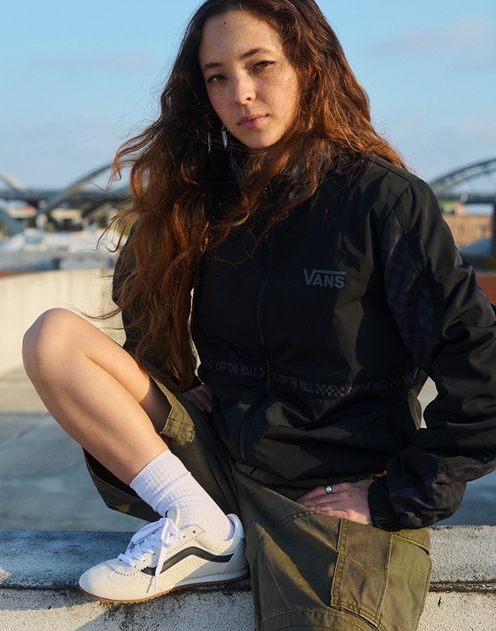 A young woman poses on a roof wearing a black hoodie, green cargo shorts, and marshmallow white Super Lowpro.