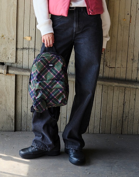 A woman poses outside a warehouse with a mauvewood MTE Hillgate Cropped Vest and a pine forest Old Skool Mini Backpack.