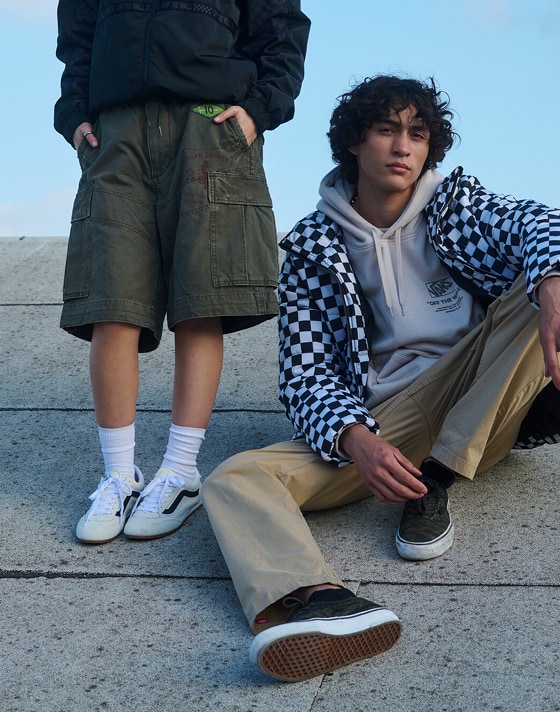 A young woman and man pose on a roof wearing Vans clothes, marshmallow white Super Lowpro, and black Authentic.