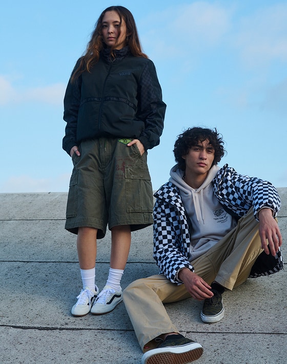 A young woman and man pose on a roof wearing Vans clothes, marshmallow white Super Lowpro, and black Authentic.