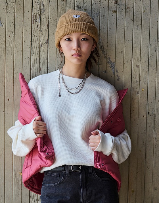 A woman poses outside of a warehouse in the mauvewood MTE HIllgate Cropped Vest and the Navigate LS Thermal Knit.