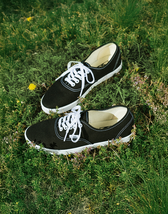 A pair of black and white Authentic lie in the grass with their laces tied.