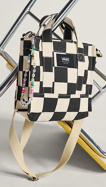 A black and white Checkerboard Lil Pergs Tote Bag hangs from a metal ladder in a photography studio.