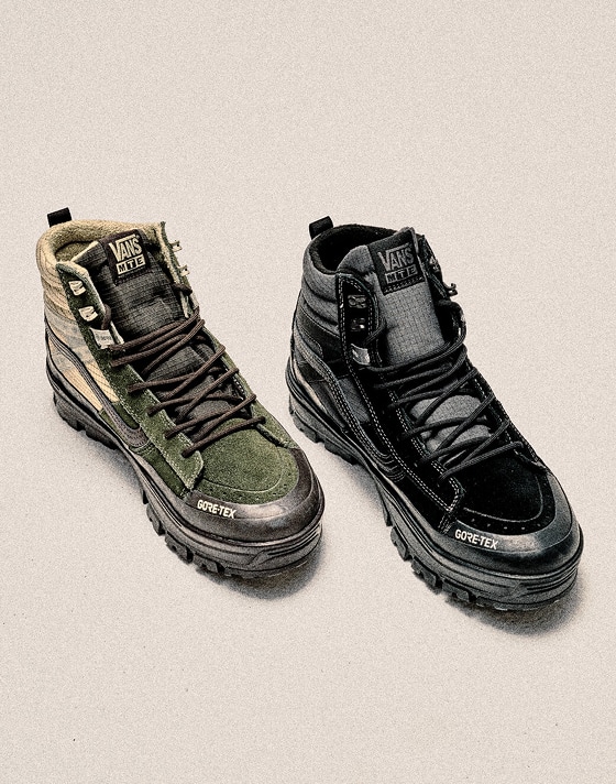 A green and white MTE Sk8-Hi GORE-TEX Insulated boots and a black one stand side-by-side in a photography studio.